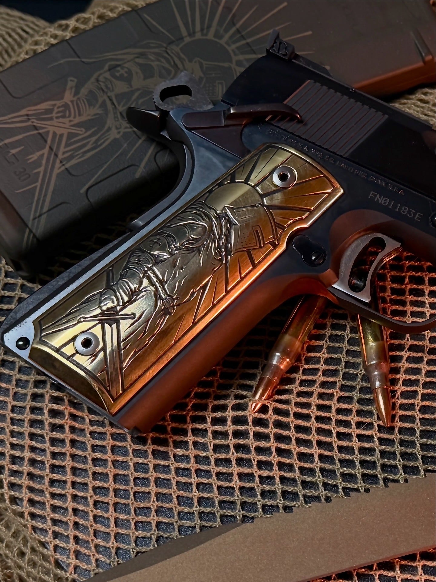 Custom 1911 with laser engraved brass grip, glock knife, and ammunition on a textured surface
