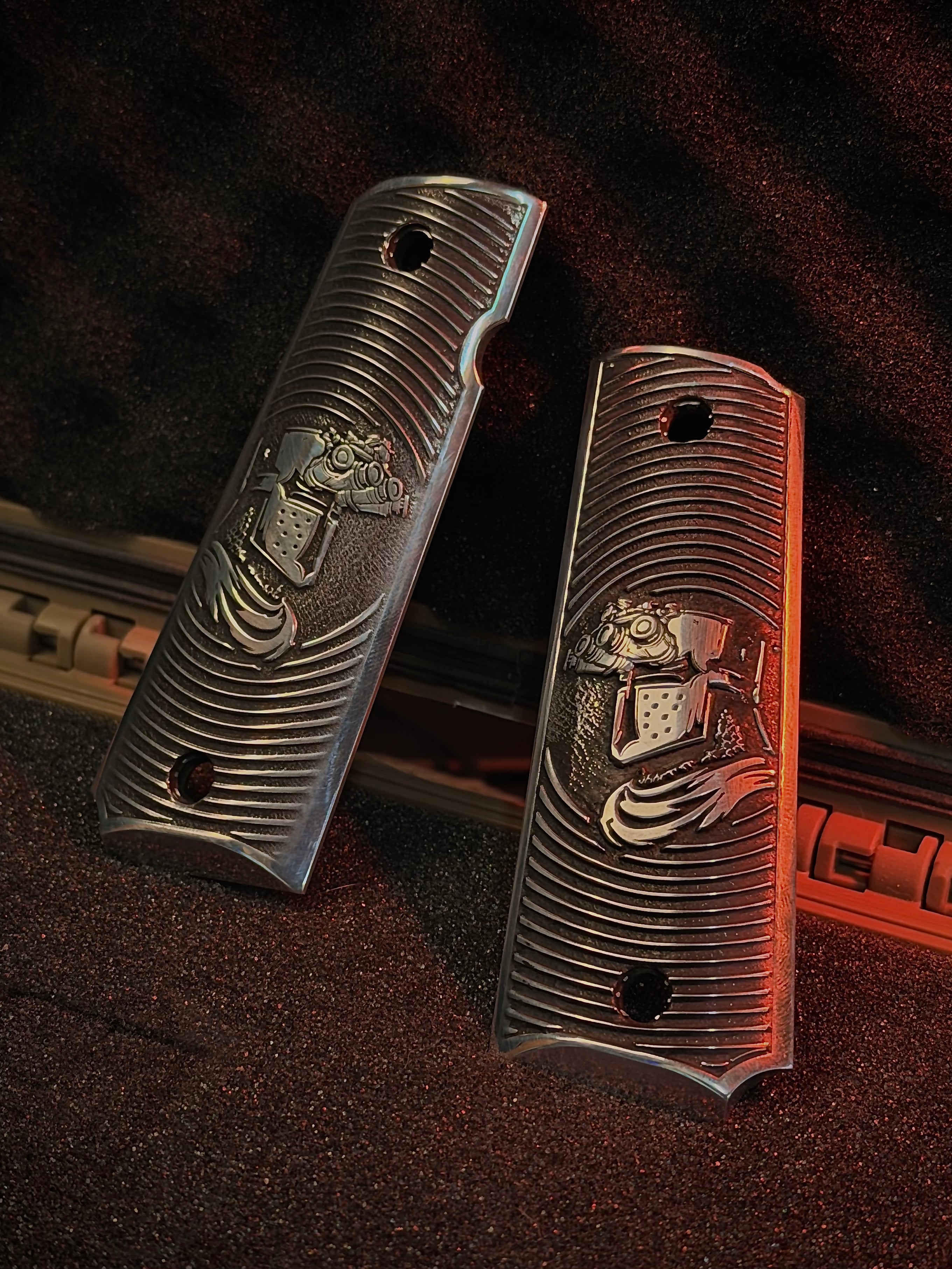 Two aluminum 1911 gun grips with engraved crusader designs on a textured surface.