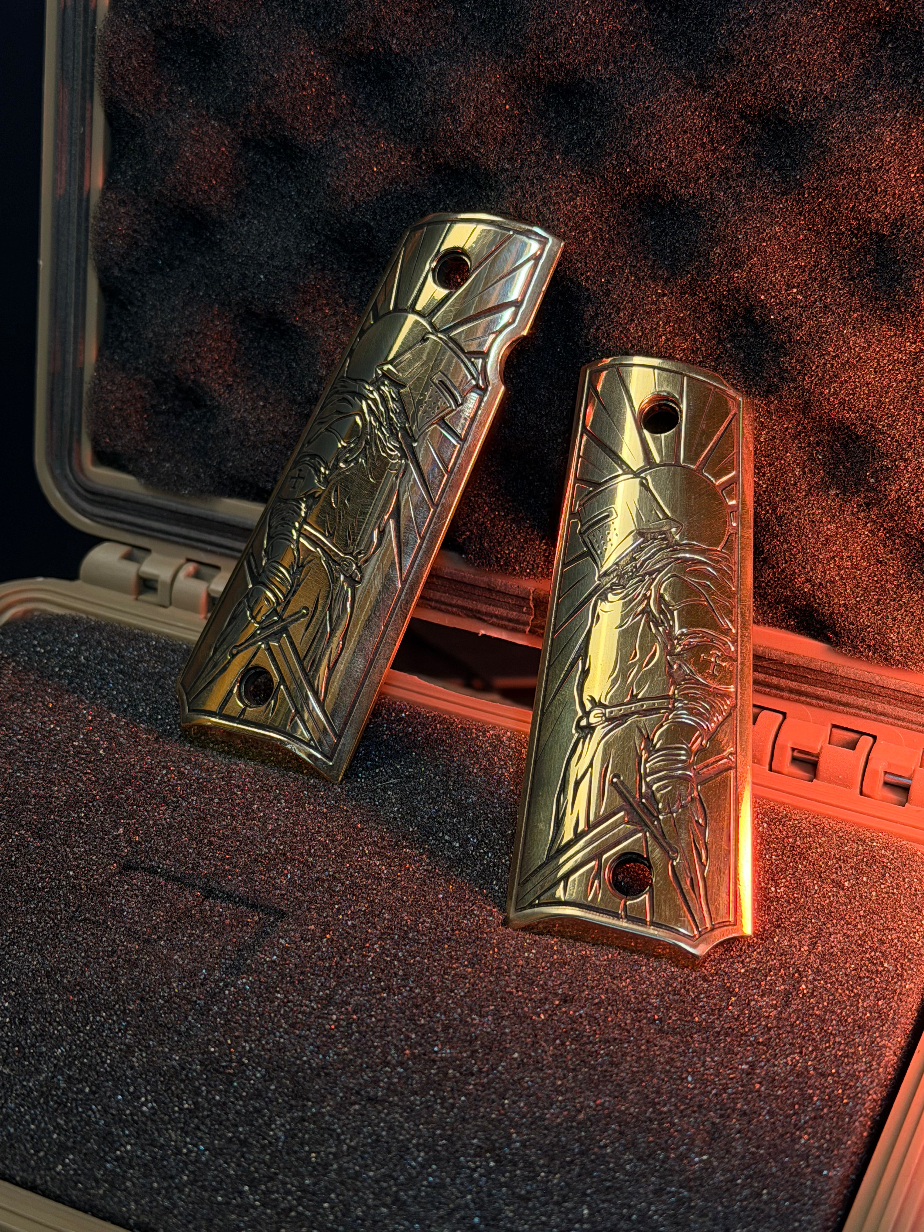 Two brass 1911 gun grips with engraved crusader designs on a textured surface.