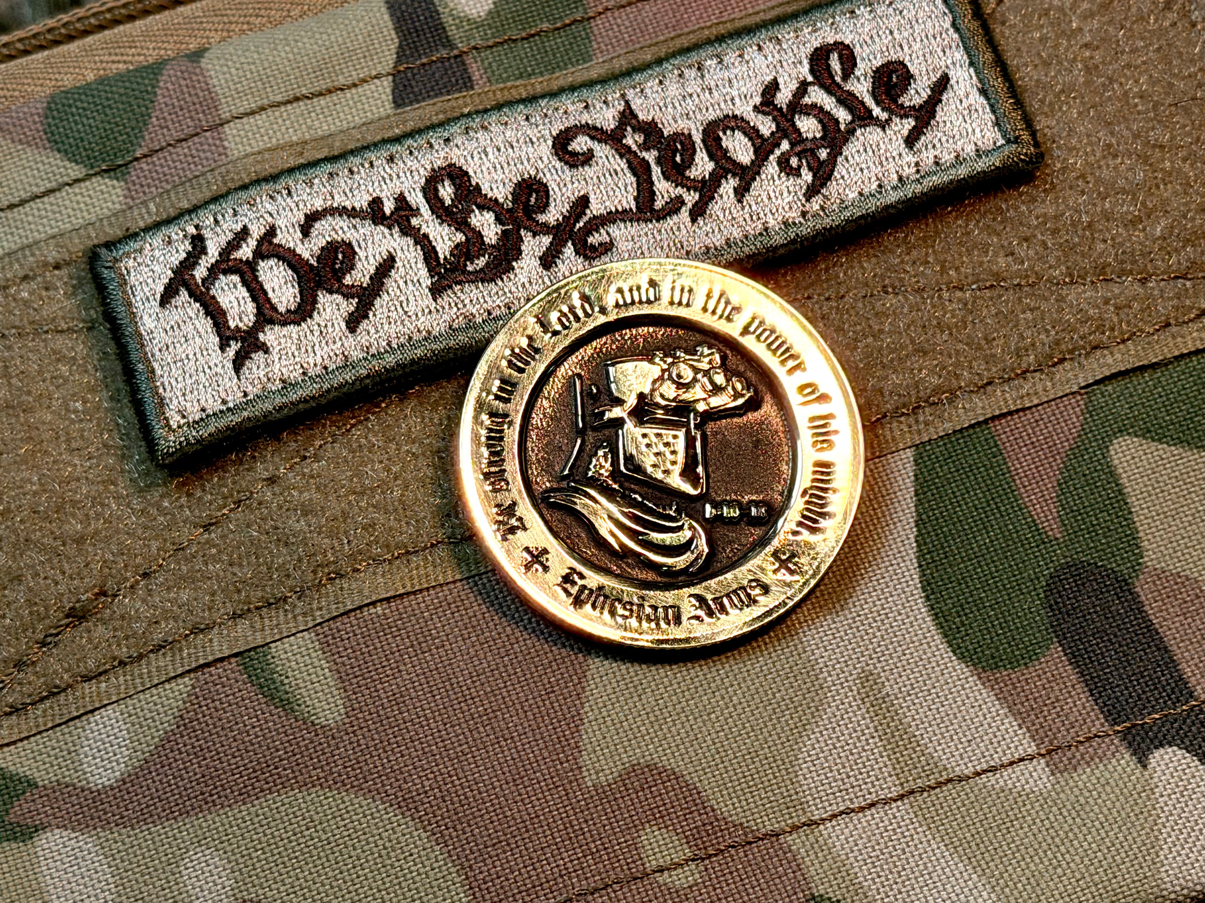 Patch with 'We the People' text and a gold coin on camouflage fabric