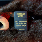 Black zippo with 'Ephesian Arms' branding and Bible verse on a fur surface